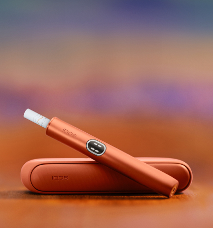 An IQOS device held by one person and a smartphone held by another person.